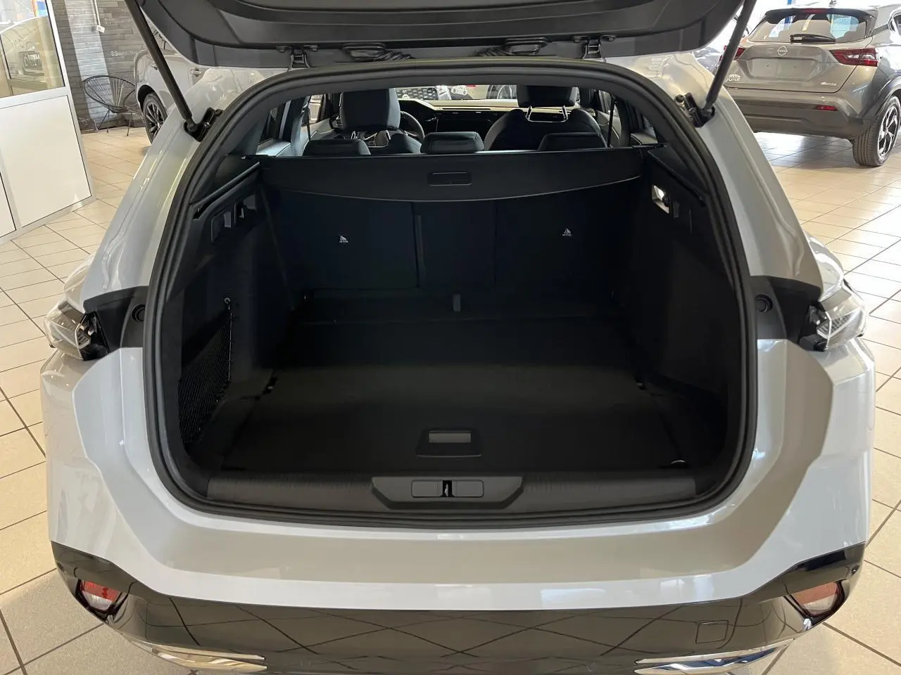 Coffre ouvert vu de l'arrière d'une Peugeot 308 SW blanc okenite avec intérieur noir et feux arrière LED griffés.