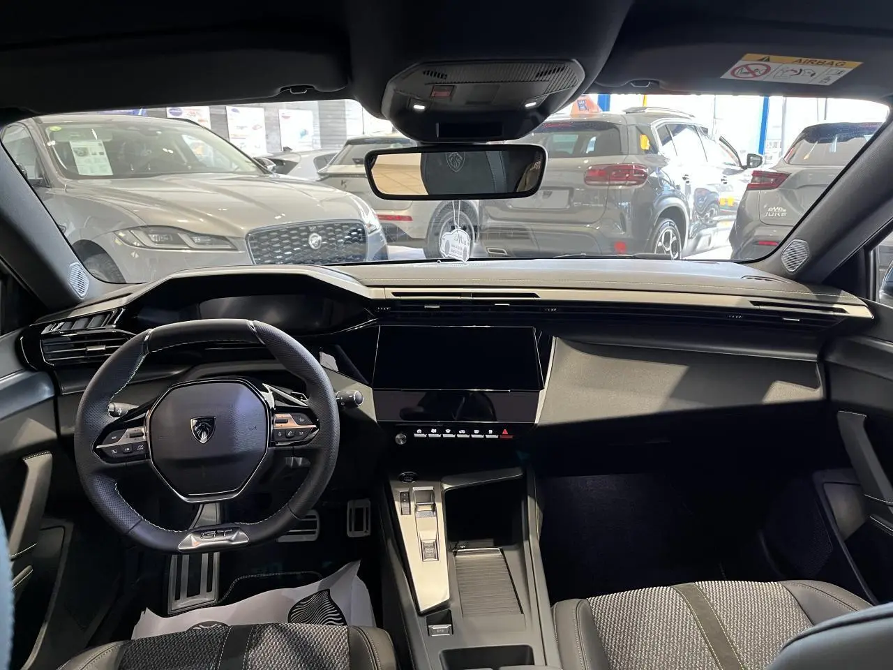 Vue intérieure avant du Peugeot 308 SW 2025 avec tableau de bord noir, volant compact et écran tactile central.