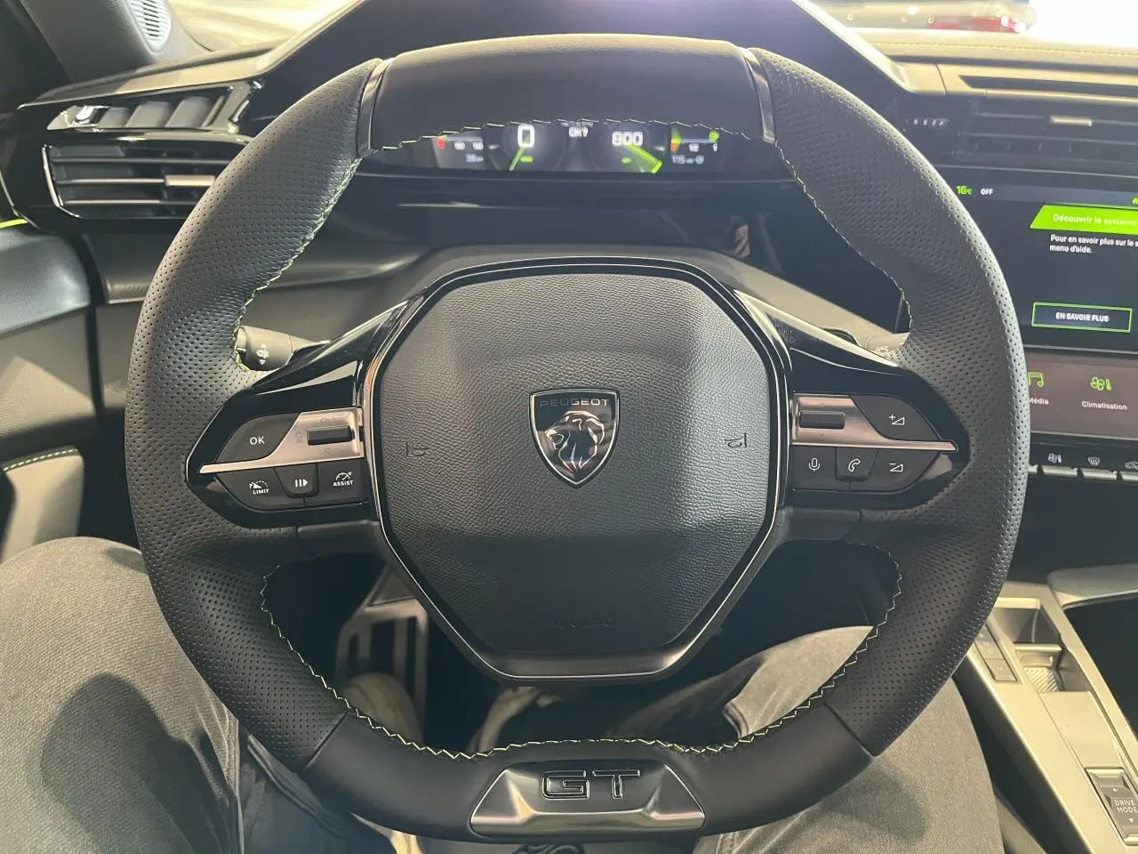 Vue rapprochée du volant cuir noir perforé avec surpiqûres vertes et badge GT de la Peugeot 308 SW 2025.