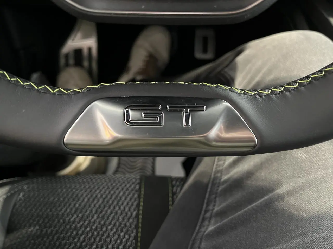 Gros plan sur le volant cuir noir avec surpiqûres vertes et logo GT en métal du Peugeot 308 SW 2025.