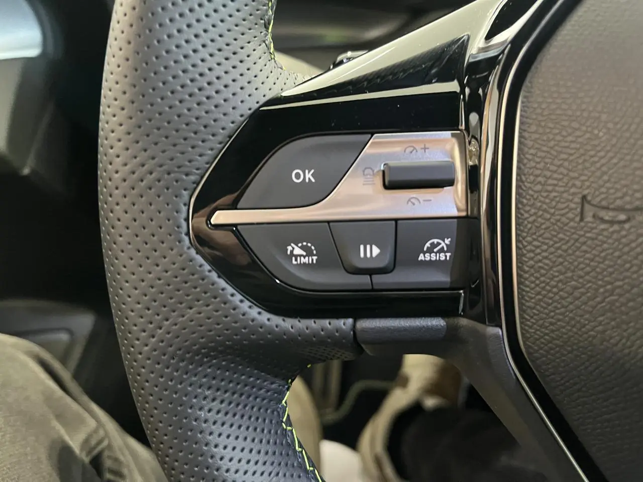 Gros plan sur les commandes à gauche du volant cuir perforé du Peugeot 308 SW blanc okenite 2025.