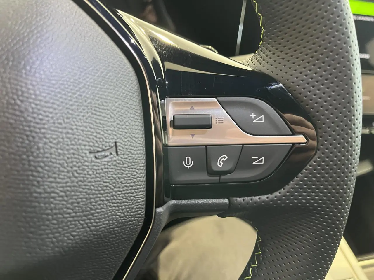Gros plan sur les commandes du volant cuir perforé de la Peugeot 308 SW GT 2025, finition noire avec surpiqûres vertes.