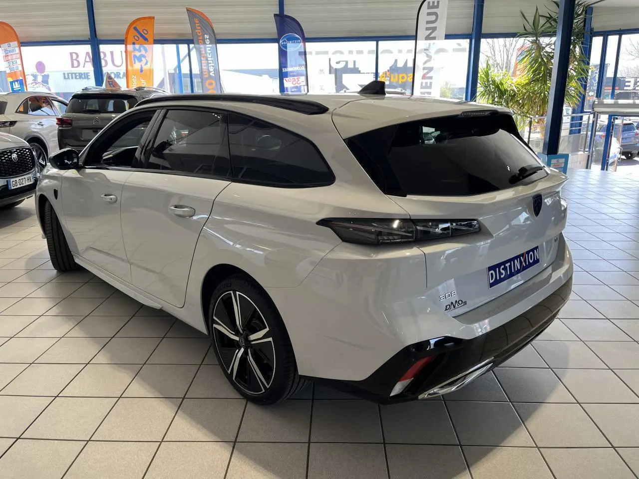 Peugeot 308 SW BlueHDi 130ch GT blanc okenite vue 3/4 arrière droit en showroom avec jantes alliage noires.
