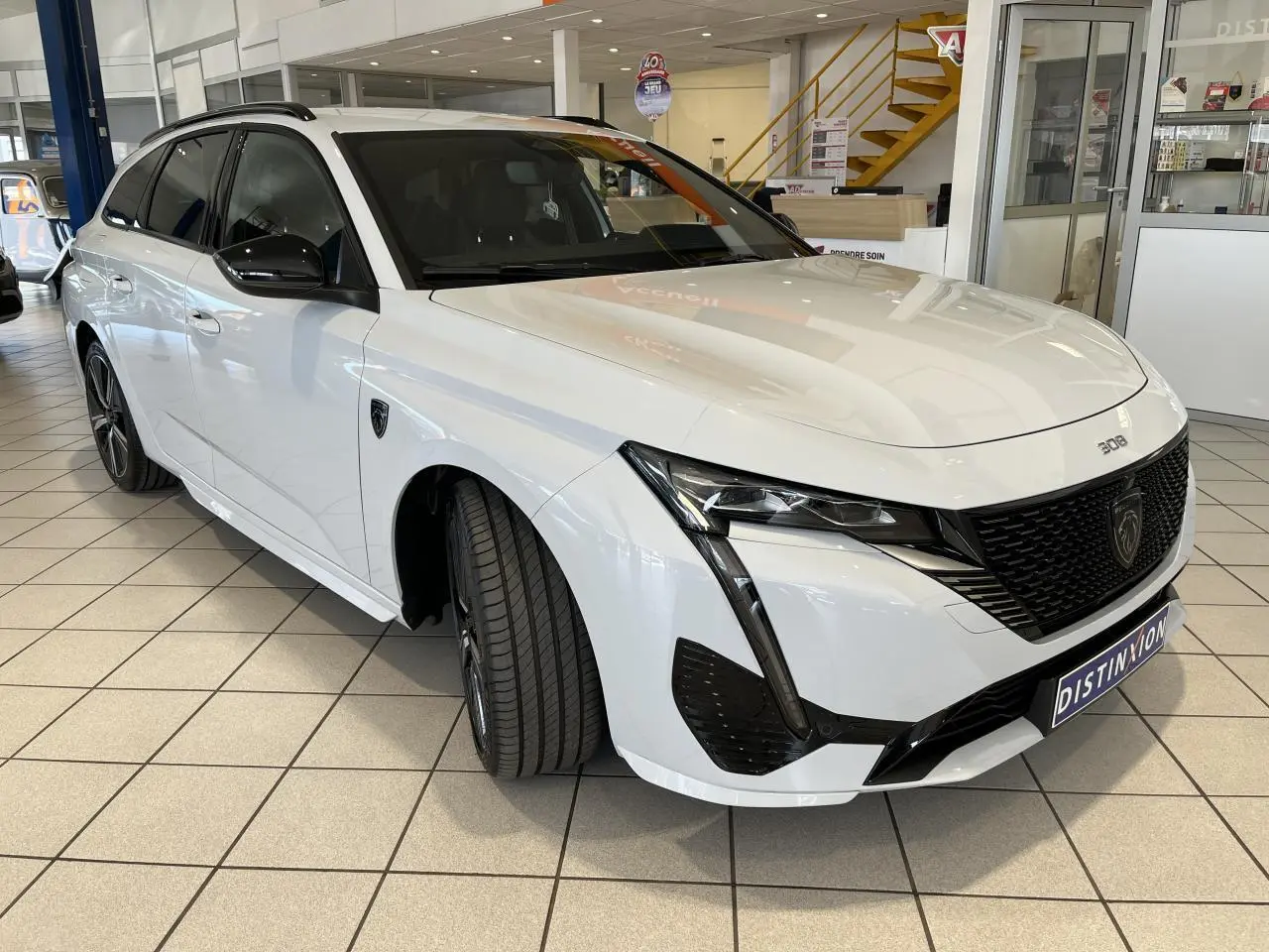 Peugeot 308 SW BlueHDi 2025 blanc okenite vue 3/4 avant droit avec calandre noire et jantes alliage 18 pouces.