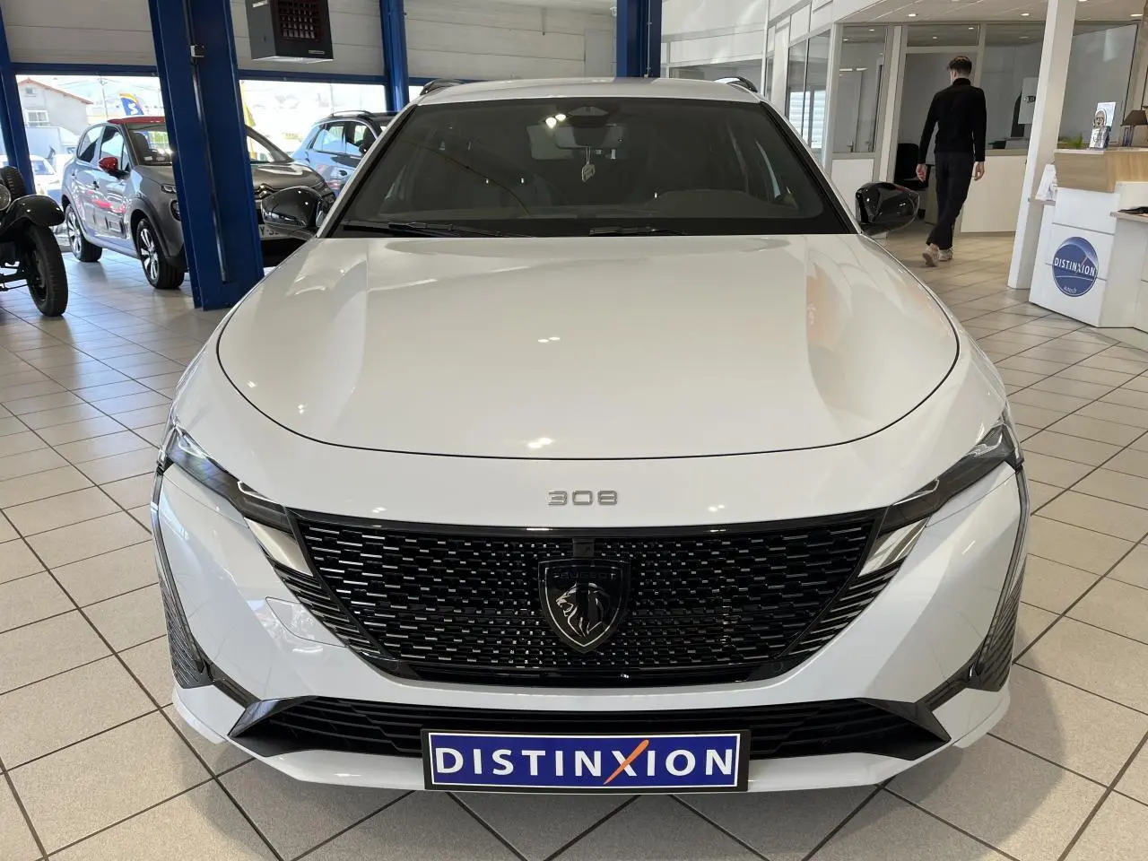 Vue frontale d'une Peugeot 308 SW blanche Okenite avec calandre noire brillante et logo lion au centre.