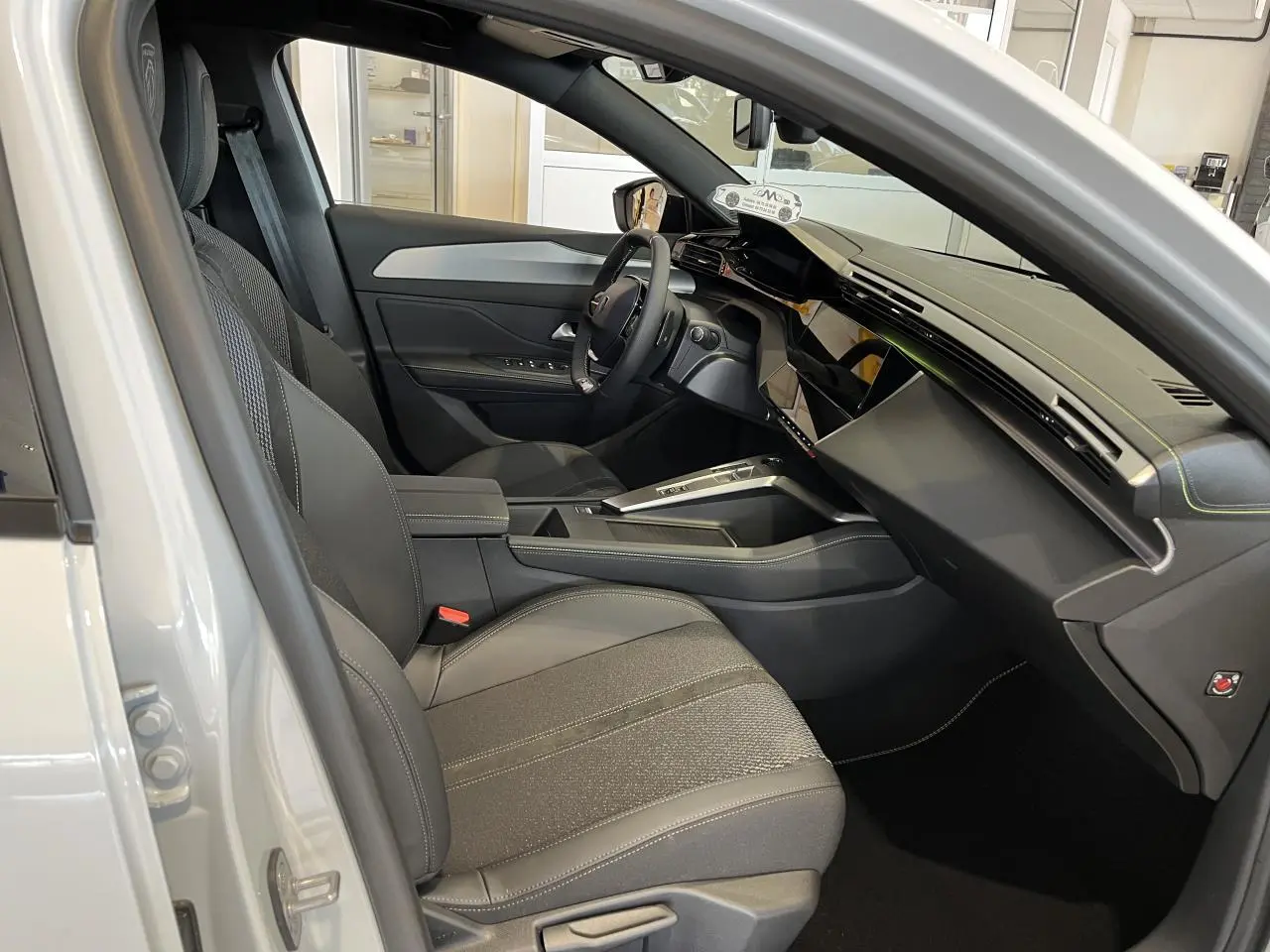 Intérieur côté conducteur d'une Peugeot 308 SW blanc okenite, avec tableau de bord moderne et sièges gris tissu et cuir.