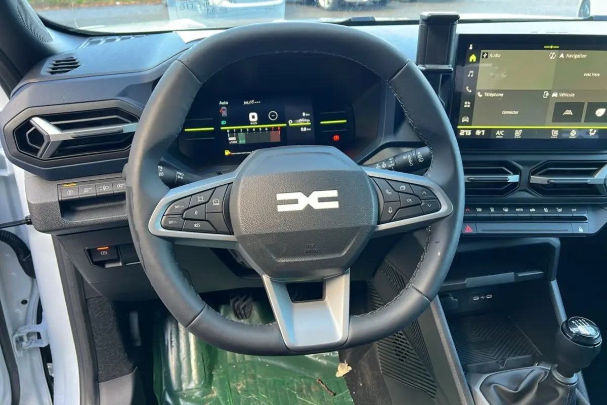 Vue intérieure centrée sur le volant et tableau de bord du Dacia Duster 2025 blanc glacier avec boîte manuelle.