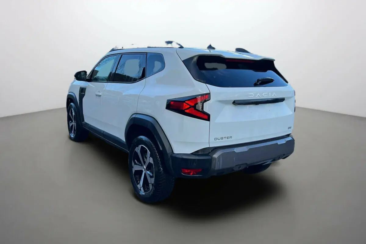 Vue 3/4 arrière du Dacia Duster blanc glacier 2025 avec ses feux arrière en forme de flèche et jantes noires distinctives.