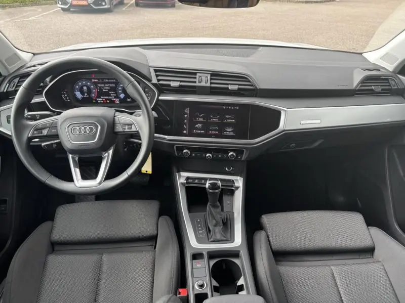 Vue intérieure de l'Audi Q3 2022 montrant le tableau de bord noir avec écran tactile et volant multifonction cuir.