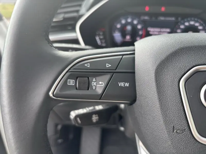 Gros plan sur les commandes gauche du volant cuir multifonction de l'Audi Q3 blanc Glacier, avec tableau de bord numérique en arrière-plan.