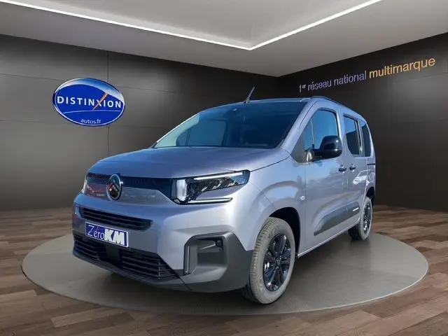 Vue 3/4 avant d'un Citroën Berlingo gris Artense avec jantes alliage noires et calandre moderne en showroom.