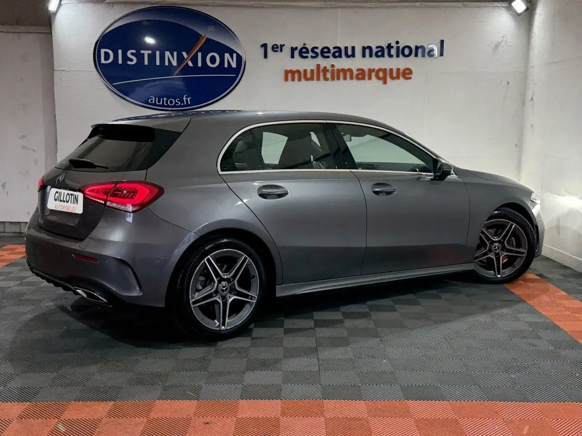 Vue latérale droite d'une Mercedes Classe A 200 AMG Line gris foncé, avec jantes alliage et feux arrière LED allumés.