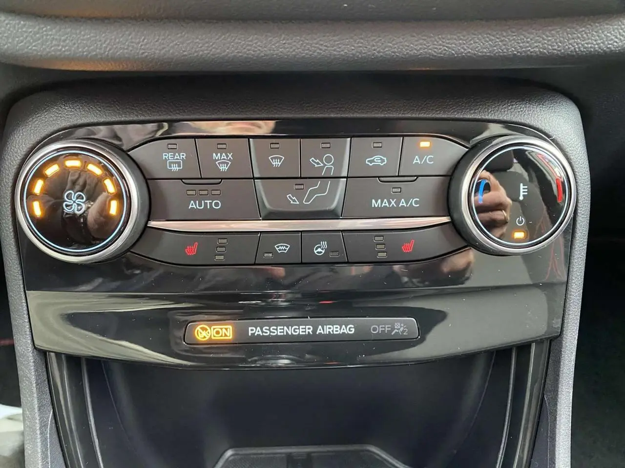 Gros plan sur la console centrale du Ford Puma rouge, montrant les commandes de climatisation et l'indicateur d'airbag passager.