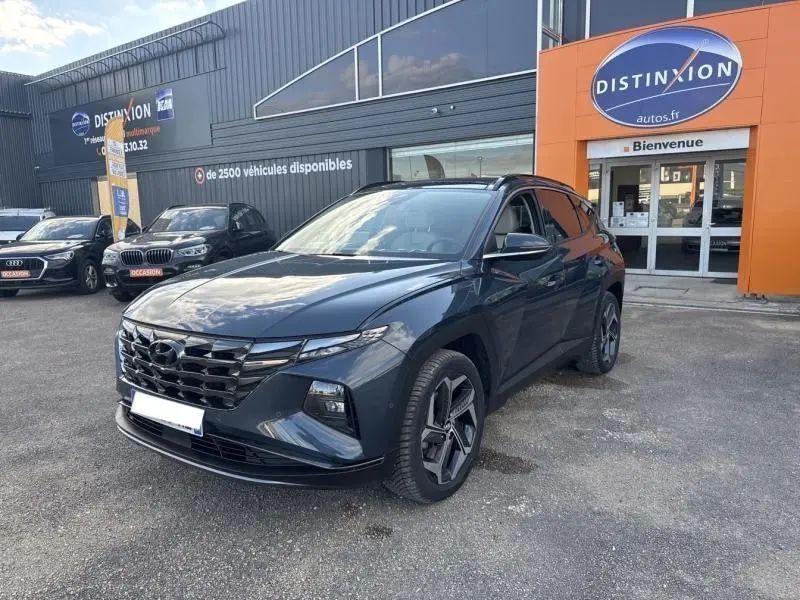 Hyundai Tucson Teal Blue Métal en 3/4 avant droit, calandre chromée et jantes alliage visibles devant un concessionnaire.