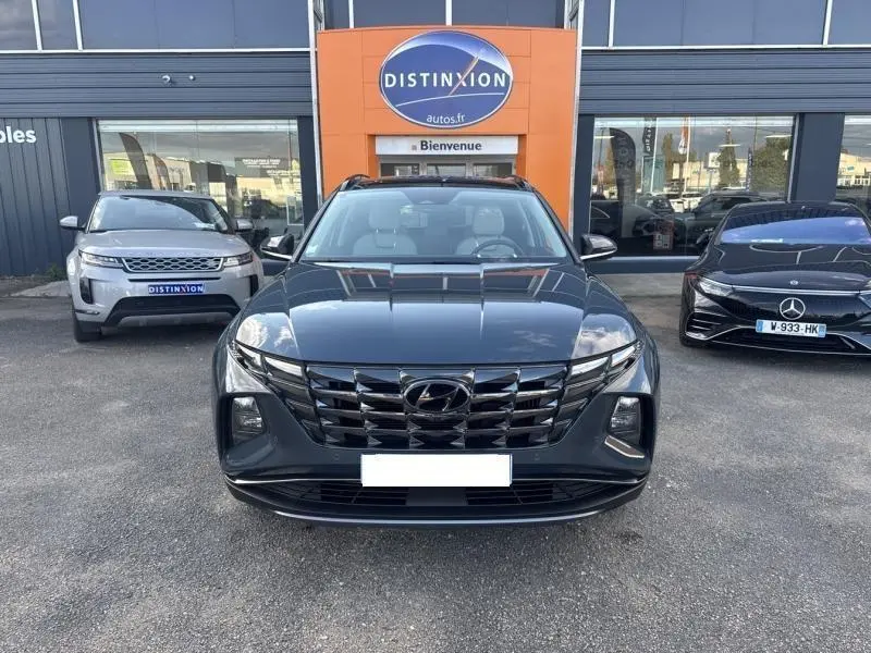 Vue frontale d'un Hyundai Tucson Teal Blue Métal avec calandre chromée et toit ouvrant panoramique visible, stationné devant un concessionnaire.