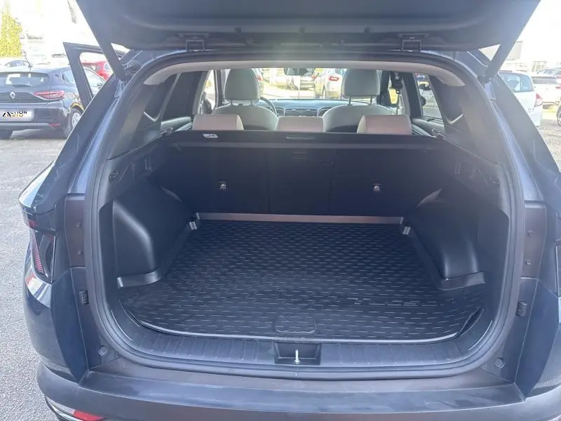 Coffre ouvert vu de l'arrière d'un Hyundai Tucson Teal Blue Métal, avec banquette arrière beige et tapis de coffre noir.