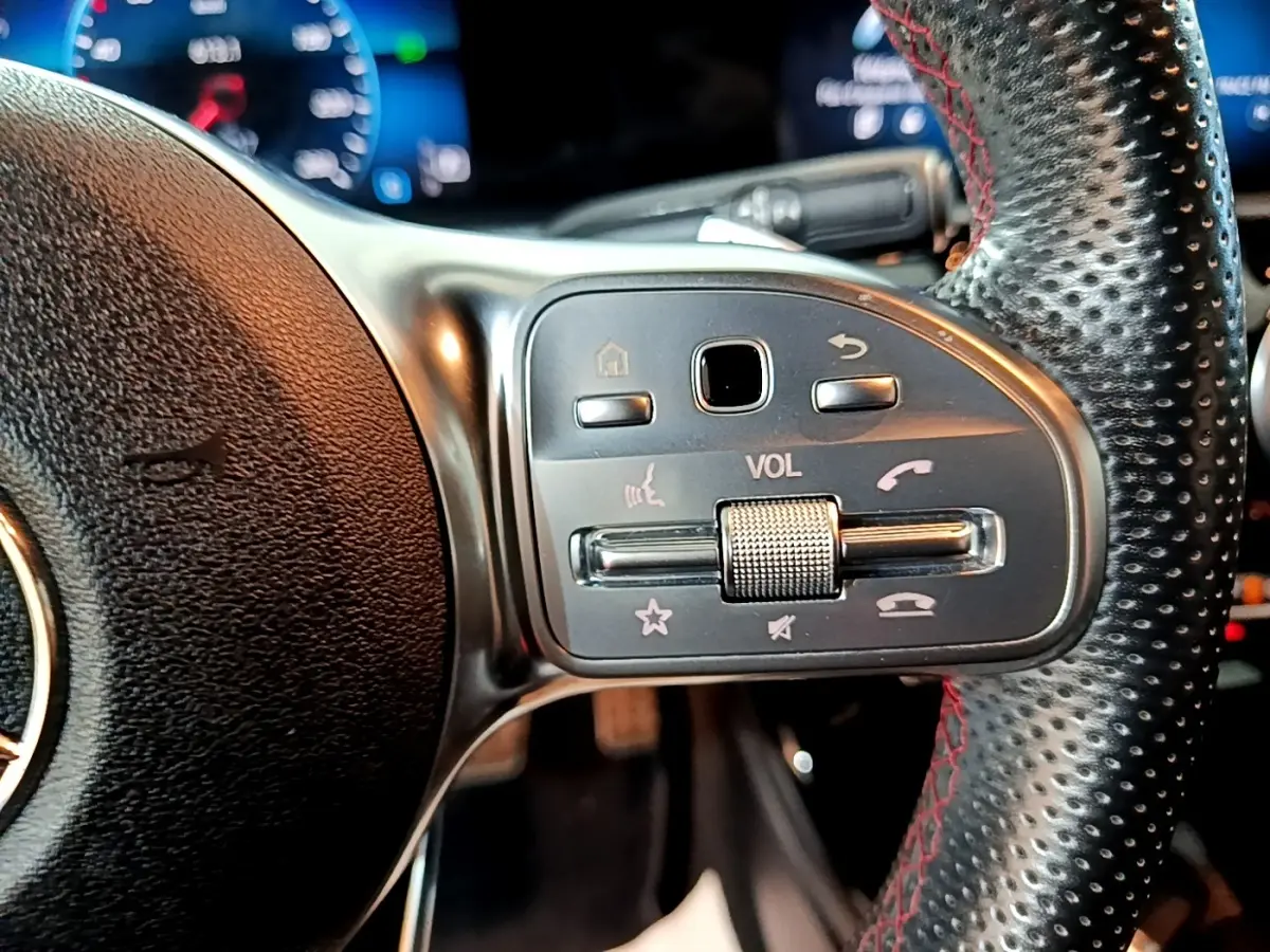 Gros plan sur les commandes de volume et téléphone du volant en cuir noir perforé avec surpiqûres rouges d'une Mercedes Classe A AMG Line 2021.