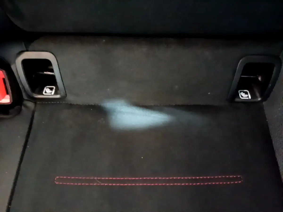 Détail du coffre arrière noir avec fixation Isofix et surpiqûres rouges visibles sur la moquette.