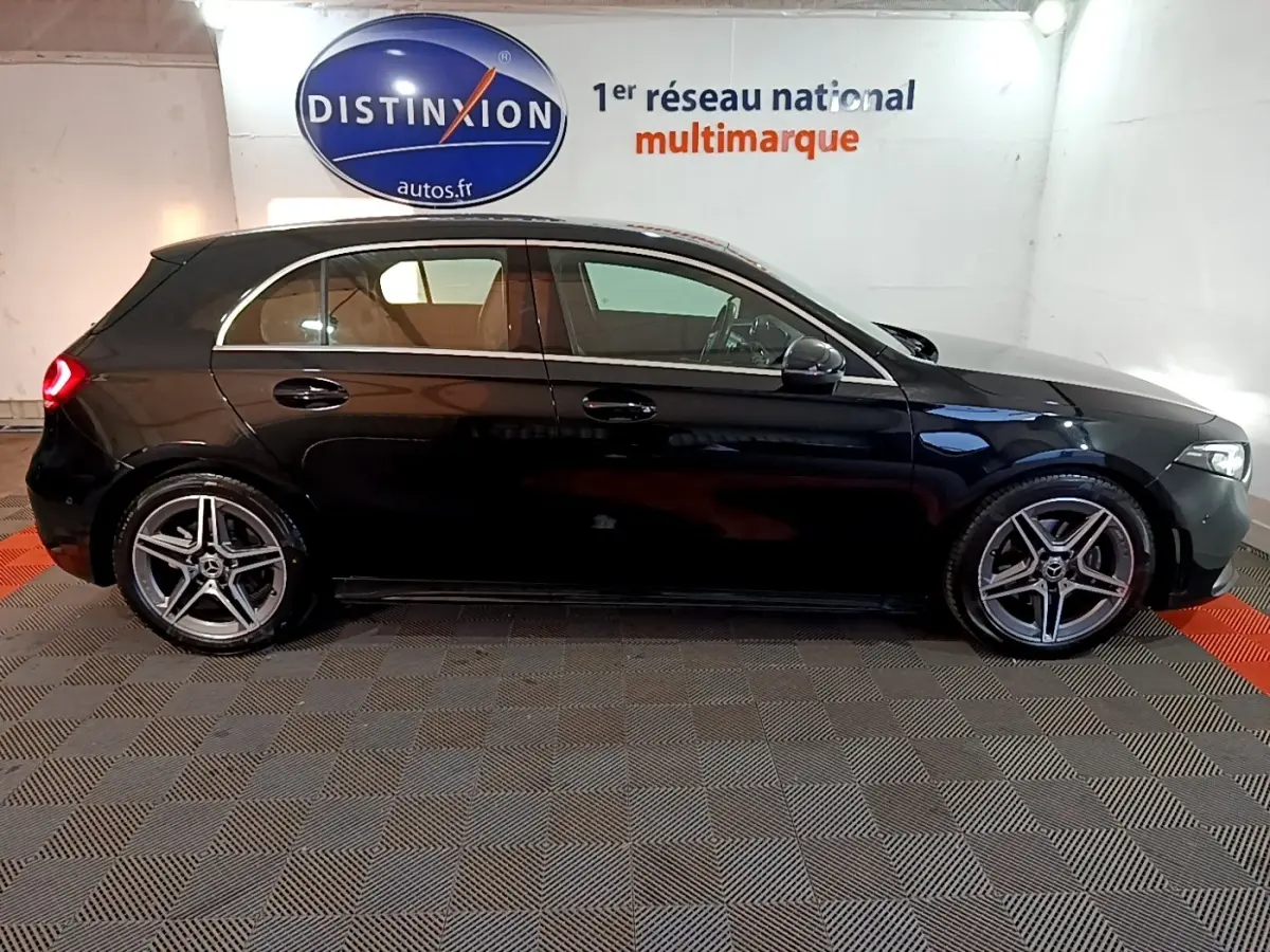 Profil droit d'une Mercedes Classe A 200 AMG Line noire, avec jantes alliage et feux arrière allumés en intérieur showroom.