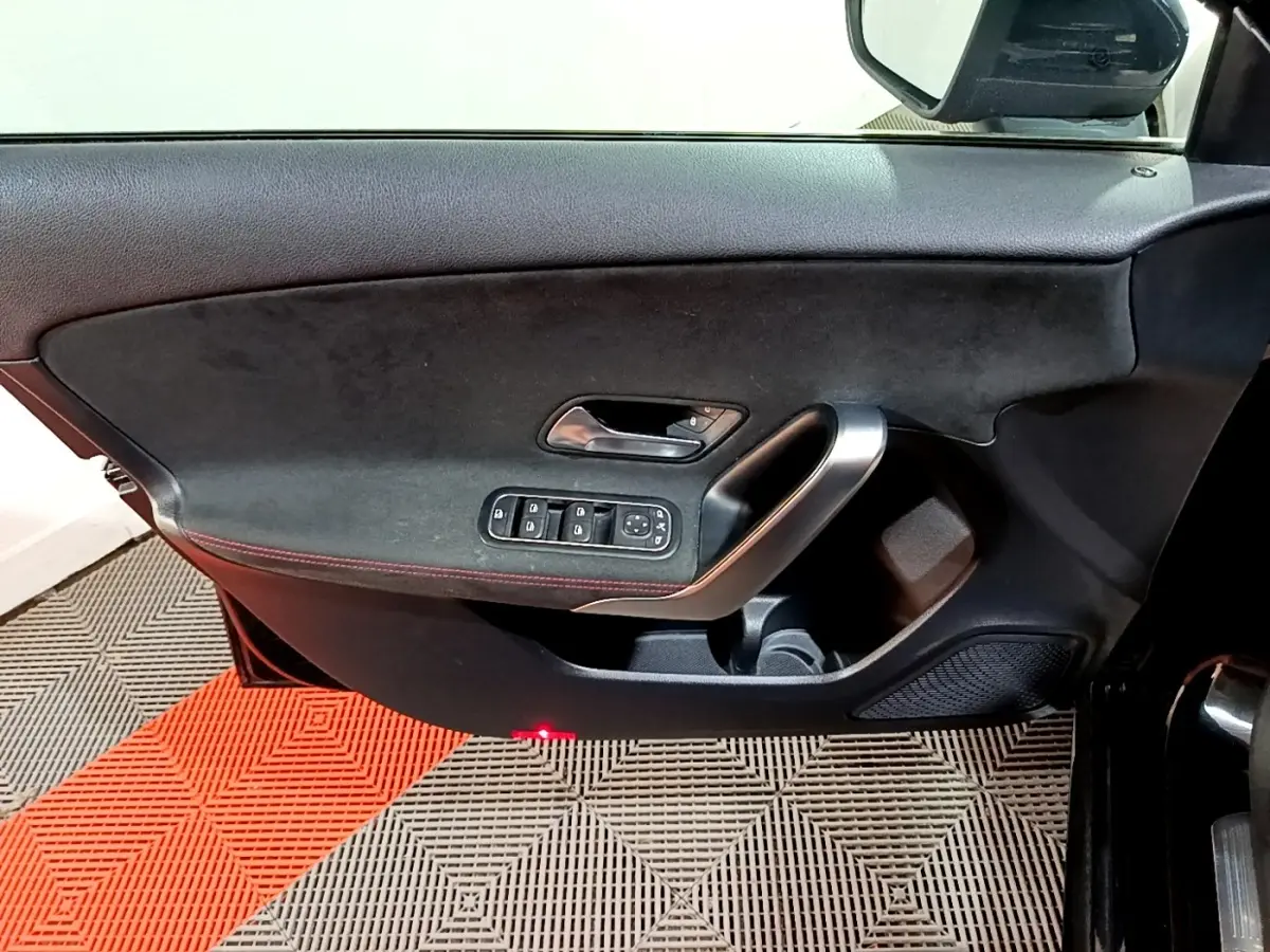 Vue rapprochée de la porte avant gauche noire de la Mercedes Classe A 200 AMG Line avec commandes électriques et surpiqûres rouges.