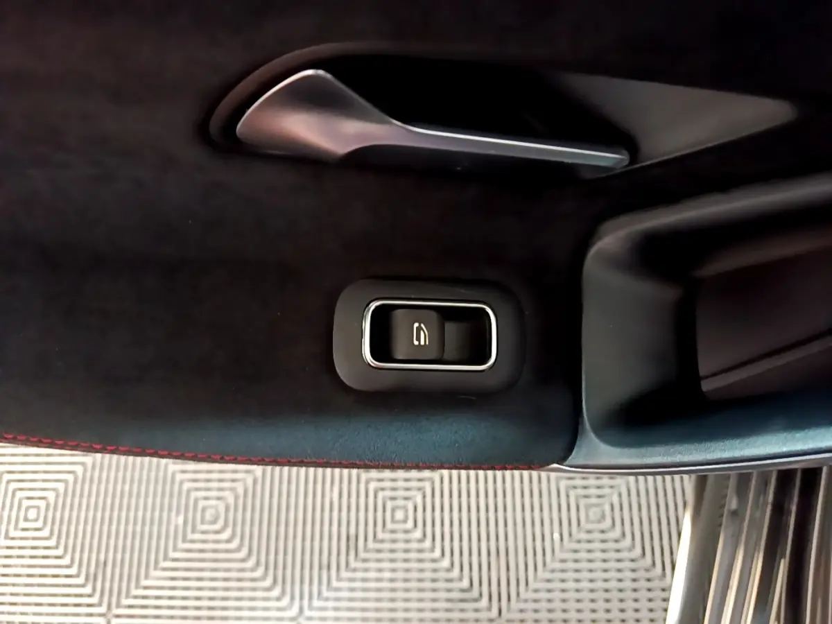 Détail intérieur montrant la commande électrique de la fermeture du coffre sur la porte côté droit, finition noire avec surpiqûres rouges.