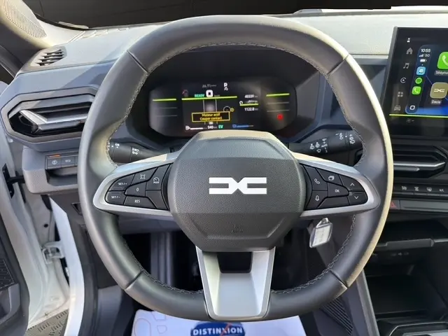 Vue rapprochée du volant cuir synthétique multifonctions du Dacia Duster Expression Hybrid 140 2025, avec tableau de bord numérique et écran tactile.