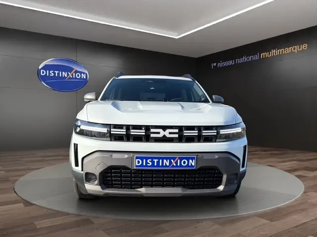 Vue de face du Dacia Duster Expression Hybrid 140 blanc, avec calandre distinctive et feux LED fins allumés.