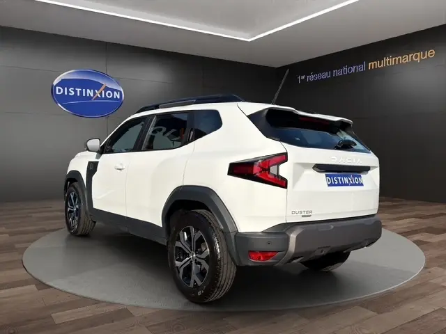 Vue 3/4 arrière droite du Dacia Duster blanc 2025 avec détails noirs et jantes alliage, en showroom.