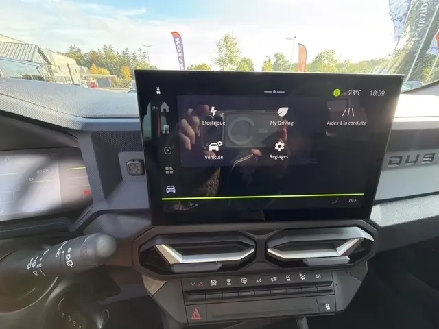 Vue intérieure du tableau de bord du Dacia Duster blanc 2025, avec écran tactile central et commandes climatisation visibles.
