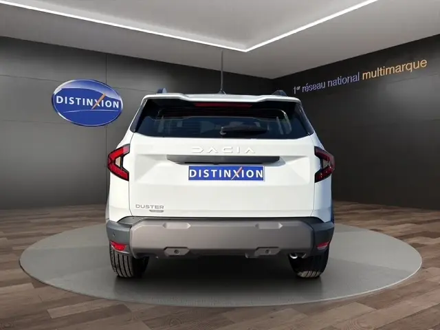 Vue arrière d'un Dacia Duster blanc 2025, version Expression Hybrid 140 avec caméra, dans un showroom.