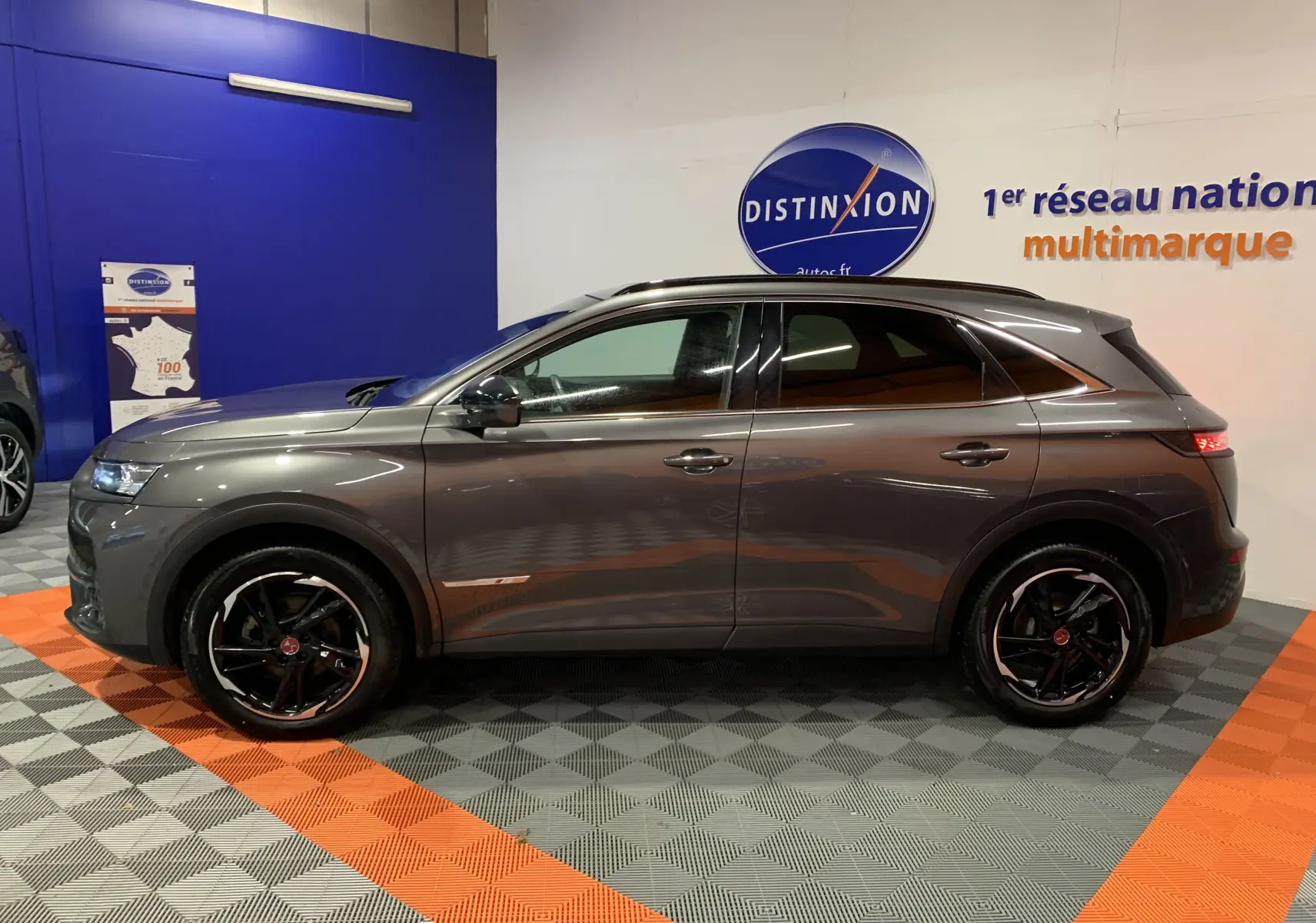 Profil côté gauche du DS7 Crossback gris Platinium 2022 avec jantes noires et toit panoramique en showroom.