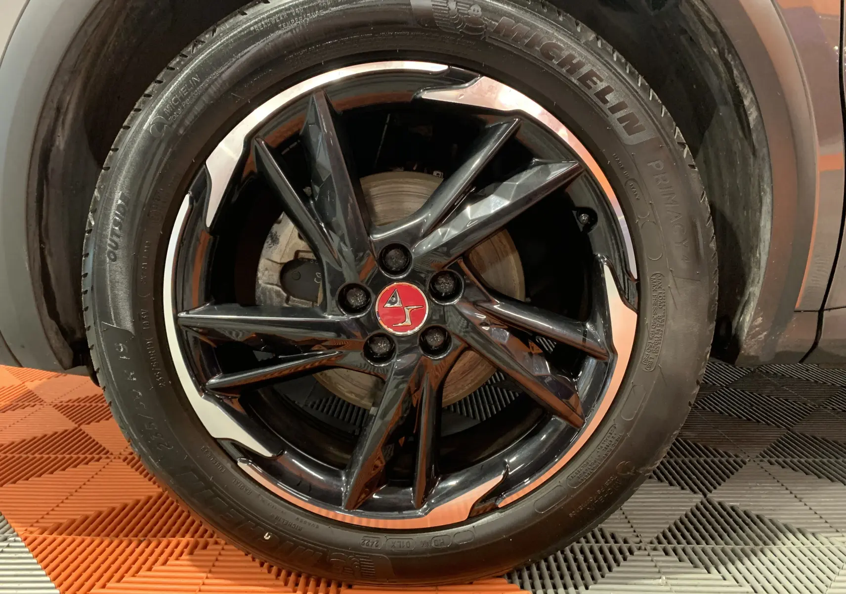 Gros plan sur la jante noire brillante avec logo rouge du DS7 Crossback Gris Platinium, pneu Michelin visible.
