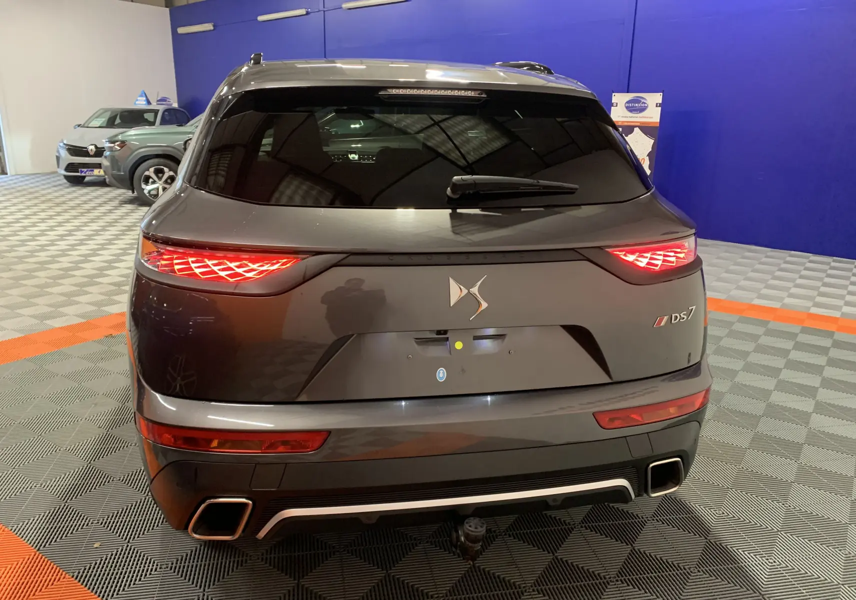 Vue arrière d'un DS7 Crossback gris Platinium avec feux arrière allumés et double sortie d'échappement carrée.