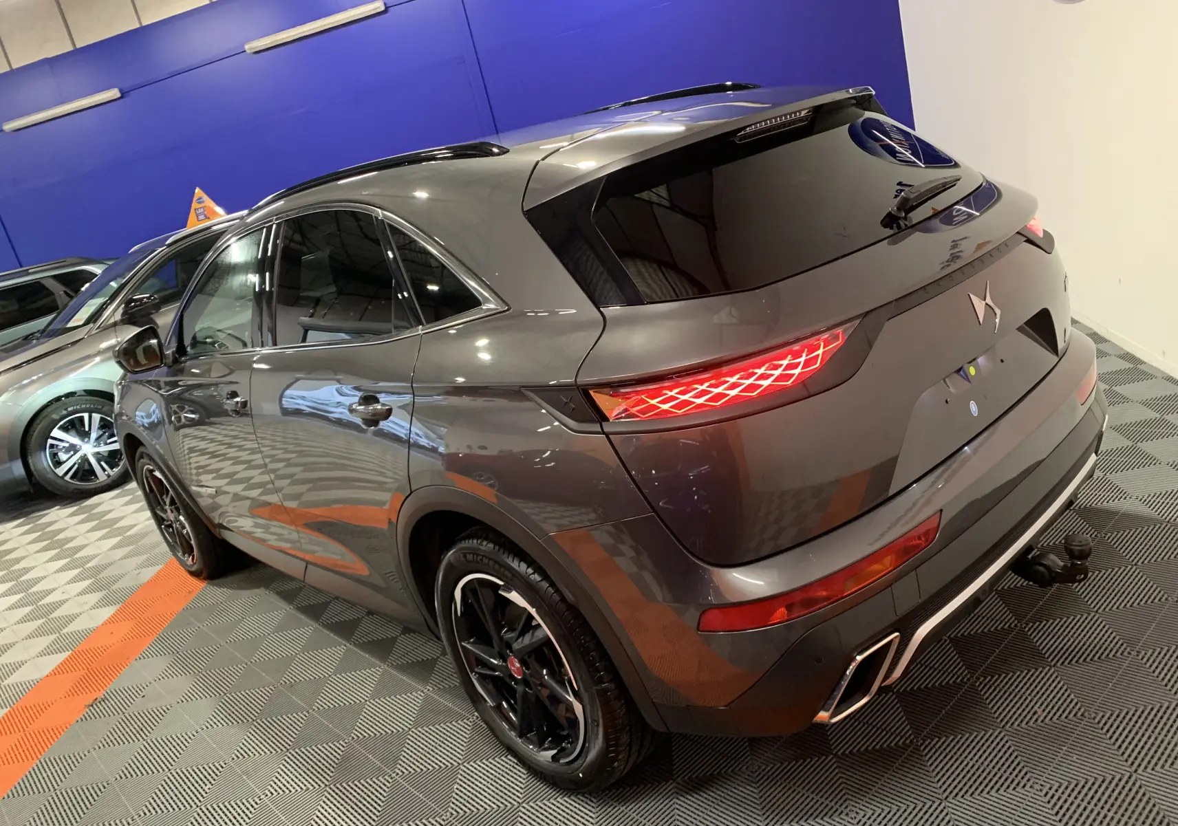Vue 3/4 arrière droite du DS7 Crossback gris Platinium avec feux arrière allumés et jantes noires brillantes.