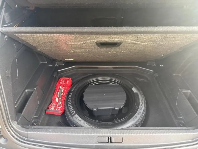 Coffre ouvert du Peugeot 3008 gris Artense, montrant la roue de secours et un kit de sécurité rouge rangé dessous.