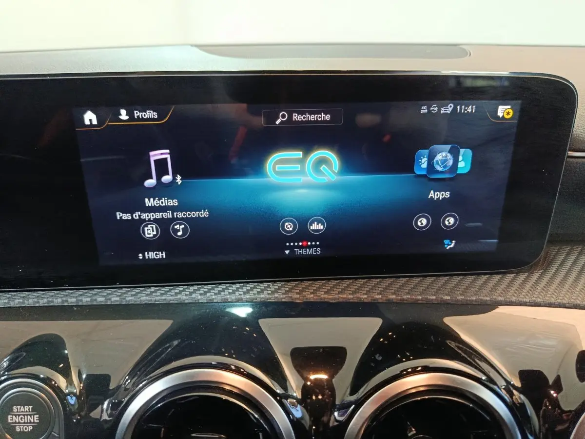 Gros plan sur l’écran tactile central et les aérateurs ronds noirs du tableau de bord de la Mercedes Classe A bleu.