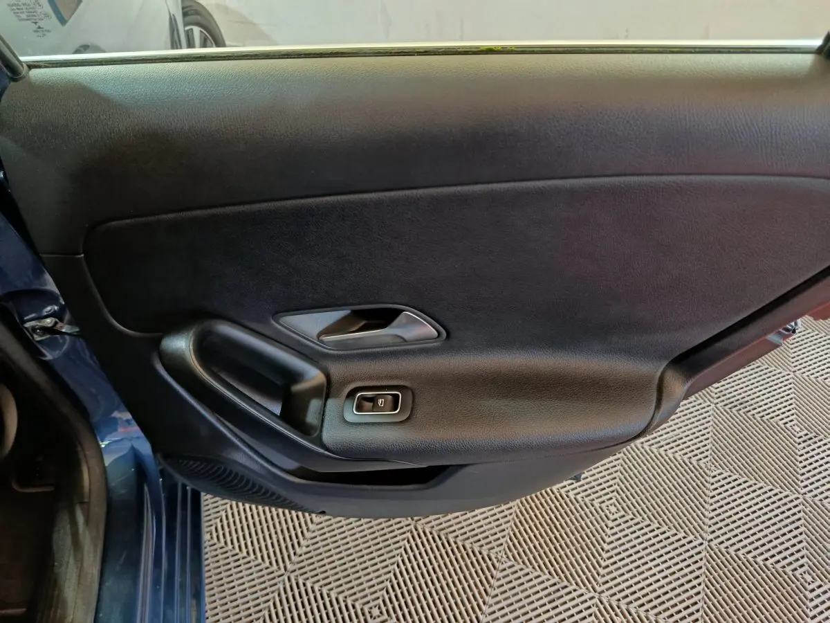 Vue intérieure côté gauche de la porte avant bleu foncé de la Mercedes Classe A 250 e Business Line avec poignée et bouton de vitre électrique.