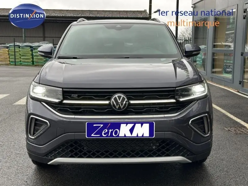 Vue avant d'un Volkswagen T-Cross gris avec calandre noire et feux LED allumés sur parking.