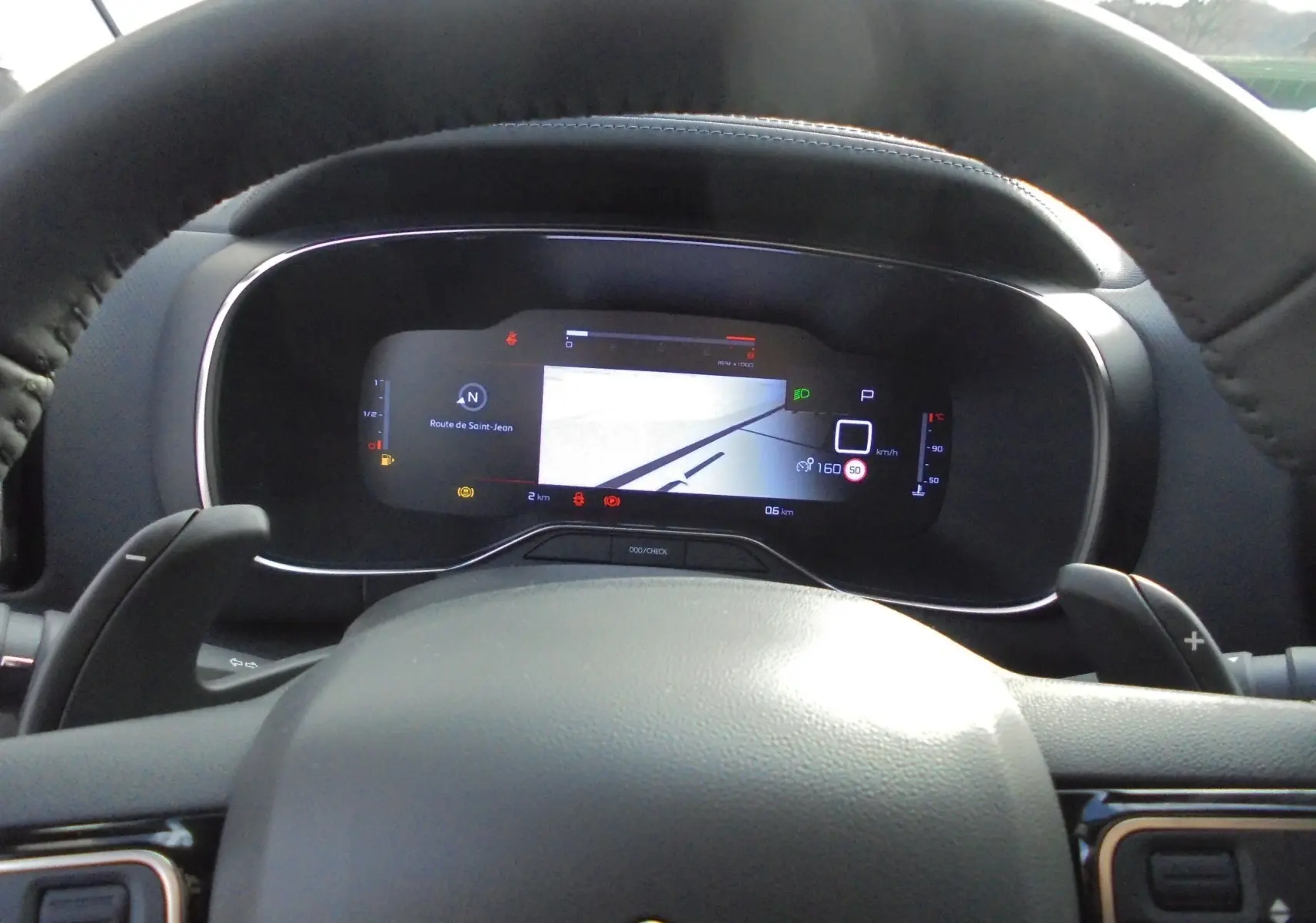 Vue rapprochée du tableau de bord numérique du Citroën C5 Aircross blanc banquise, affichant la navigation et les indicateurs de conduite.