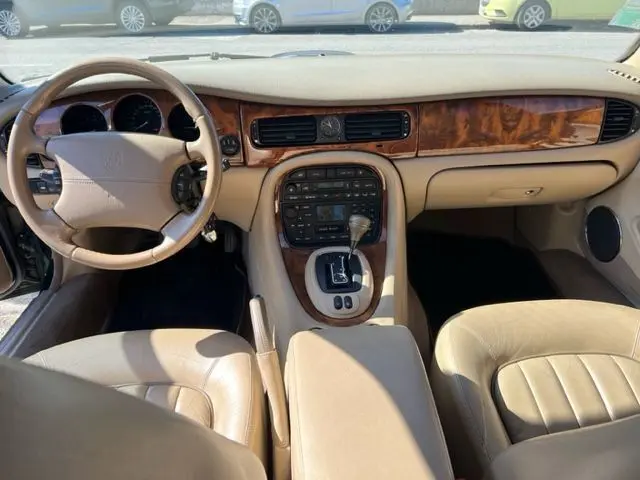 Vue intérieure avant de la Jaguar Sovereign 3.2 V8 2002, montrant le tableau de bord en bois et cuir beige avec boîte automatique.