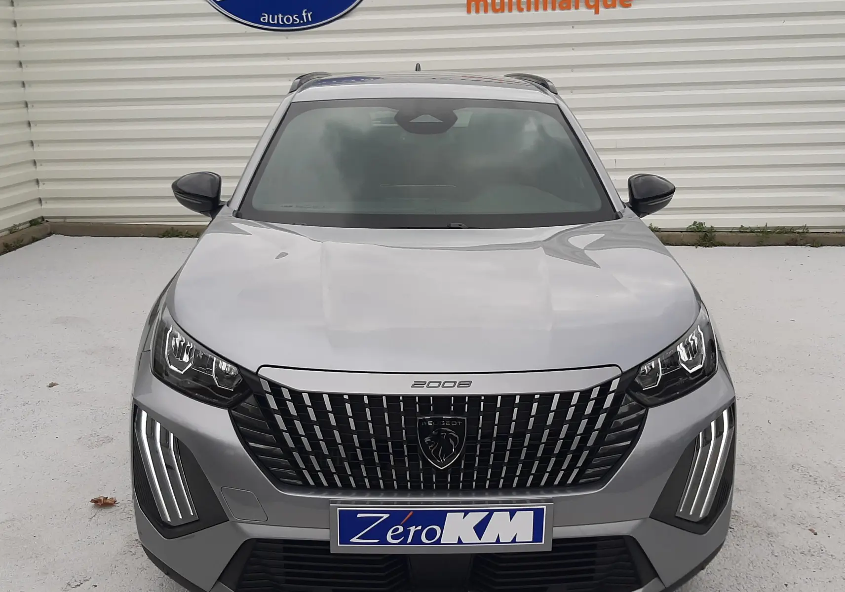 Vue frontale d'un Peugeot 2008 gris Artense avec calandre noire et feux LED verticaux allumés.