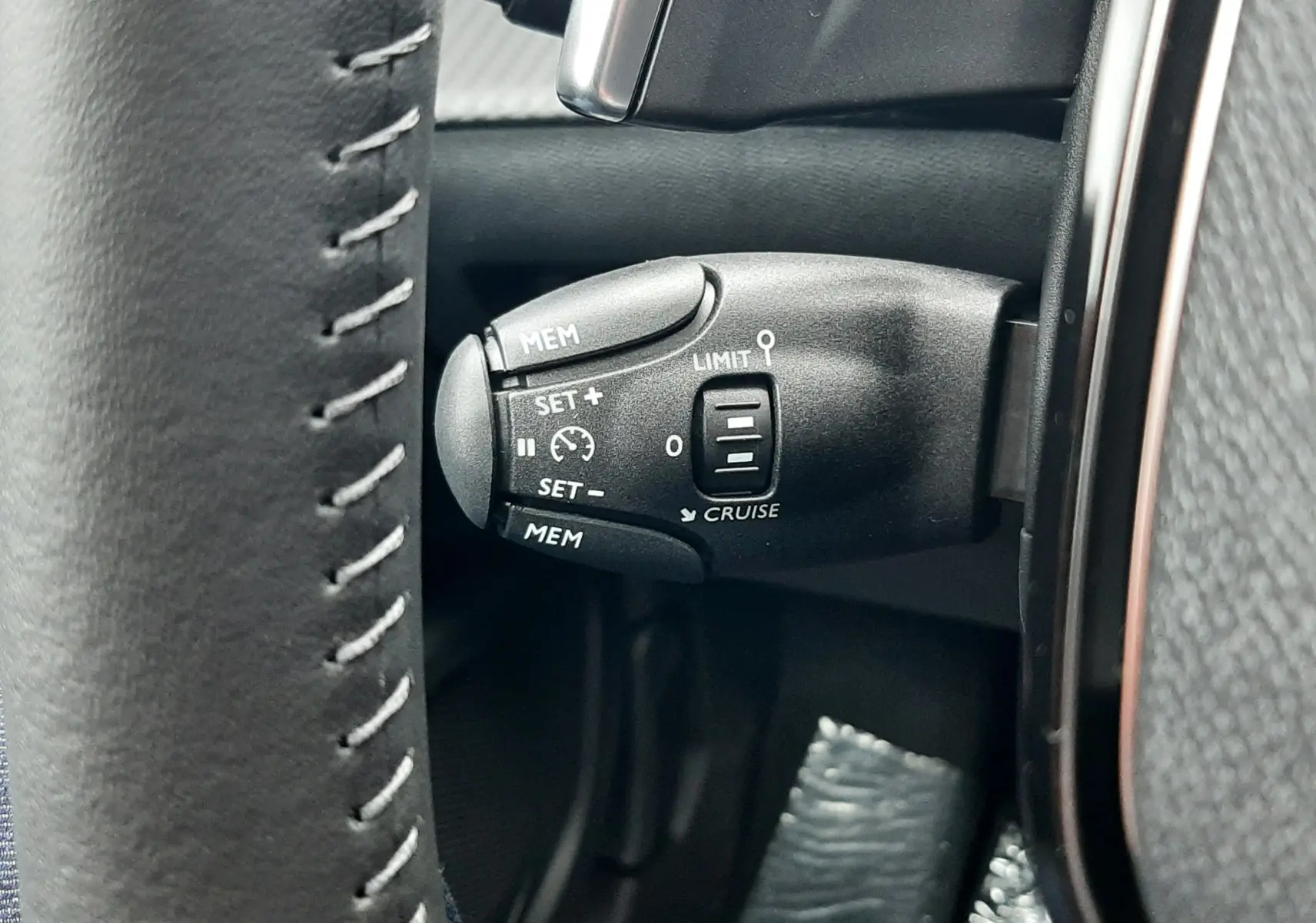 Gros plan sur la commande de régulateur de vitesse à gauche du volant cuir gris du Peugeot 2008 hybride 2025.