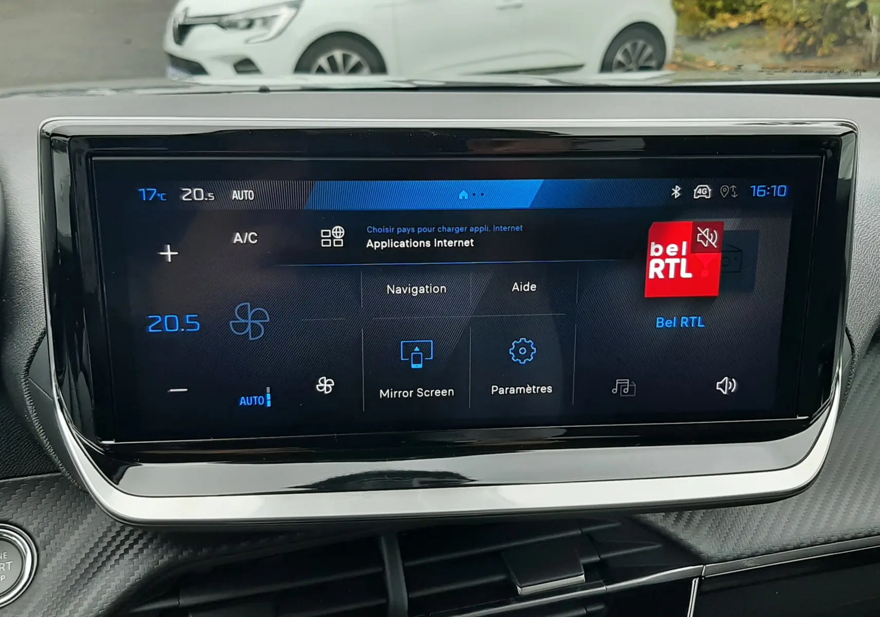 Écran tactile central du Peugeot 2008 2025 affichant le menu navigation et climatisation, avec une voiture blanche en arrière-plan.