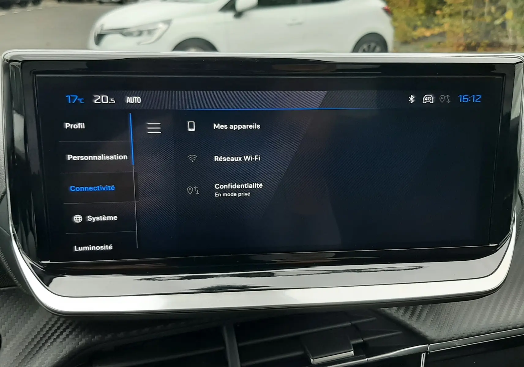 Écran tactile central du Peugeot 2008 gris Artense, affichant les options de connectivité, avec une voiture blanche en arrière-plan.
