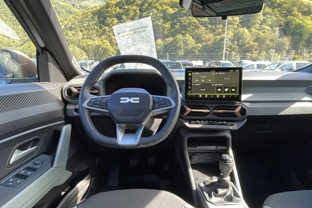 Intérieur du Dacia Bigster 2025 essence gris schiste, vue frontale du poste de conduite avec volant et écran tactile.