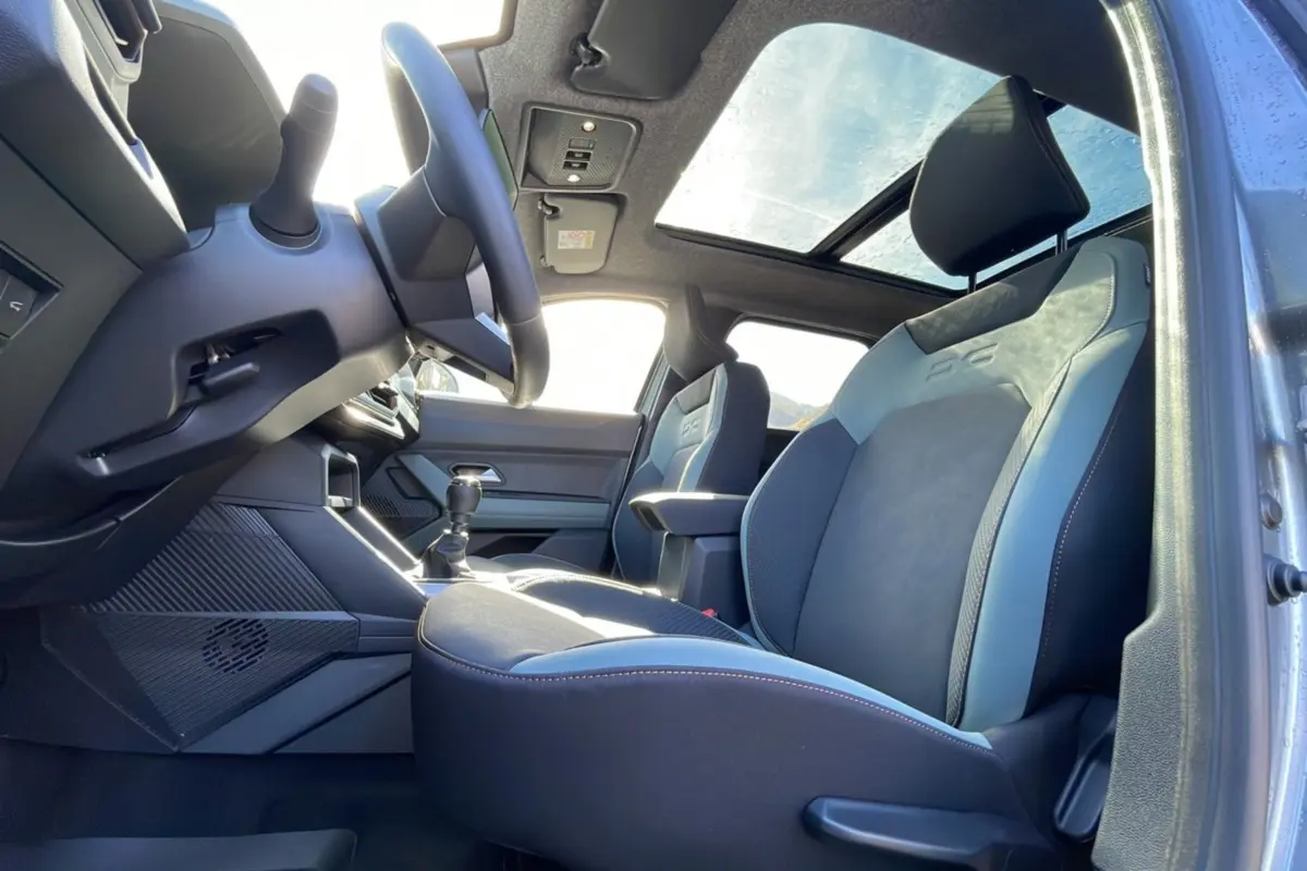 Vue intérieure côté conducteur du Dacia Bigster 2025 gris schiste, sièges avec logo et toit panoramique lumineux.