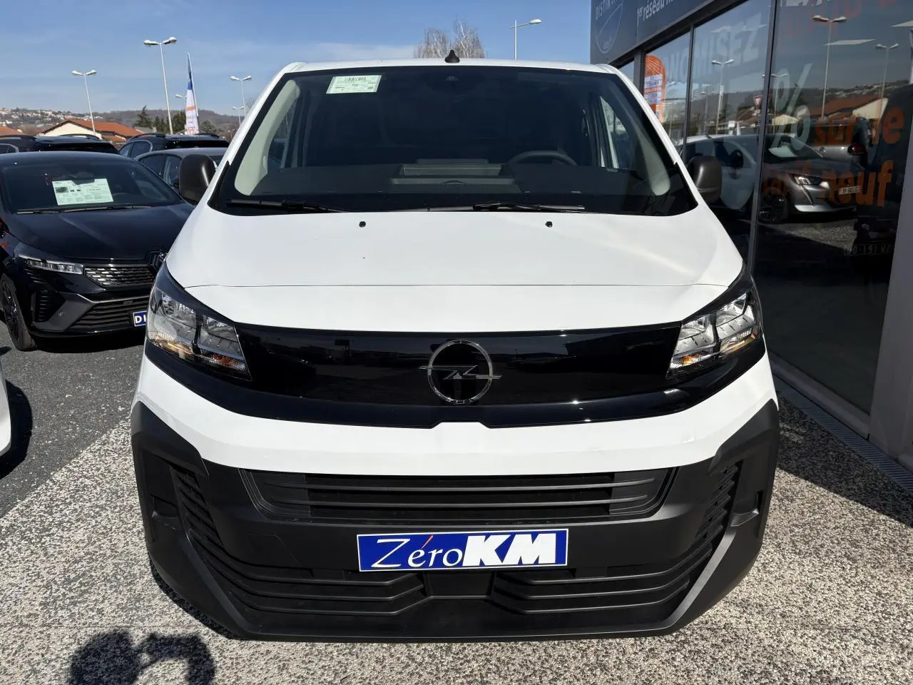 Vue frontale d'un Opel Vivaro blanc 2024 avec calandre noire et plaque "Zéro KM" en concession.
