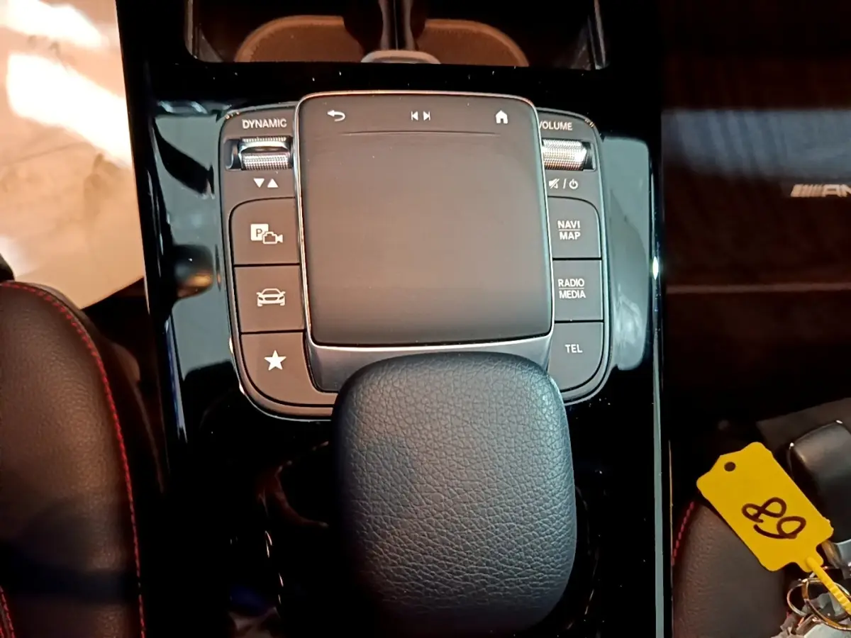 Gros plan sur la console centrale noire brillante de la Mercedes Classe A 250 e AMG Line avec pavé tactile et accoudoir cuir.