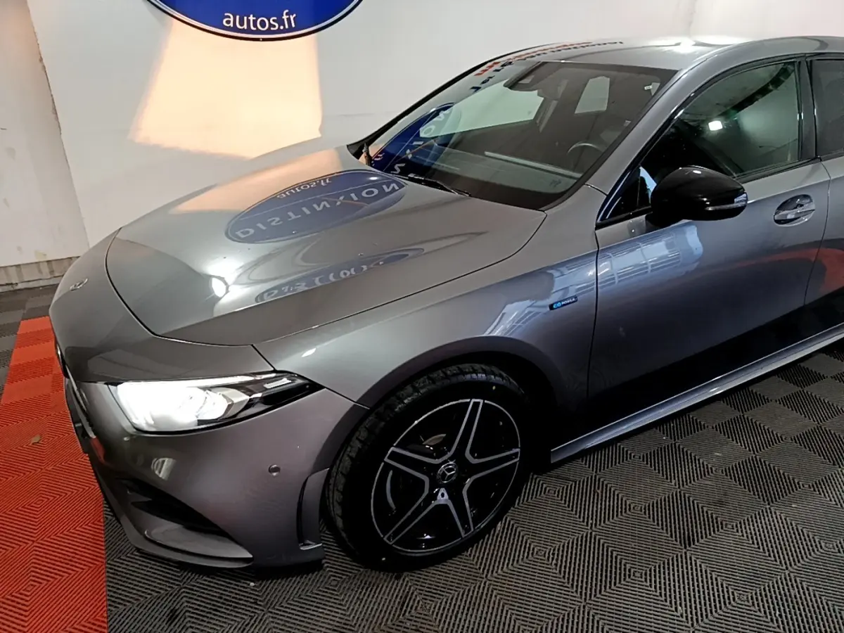 Mercedes Classe A 250 e AMG Line gris foncé vue 3/4 avant droit, avec jantes noires et phares LED allumés.