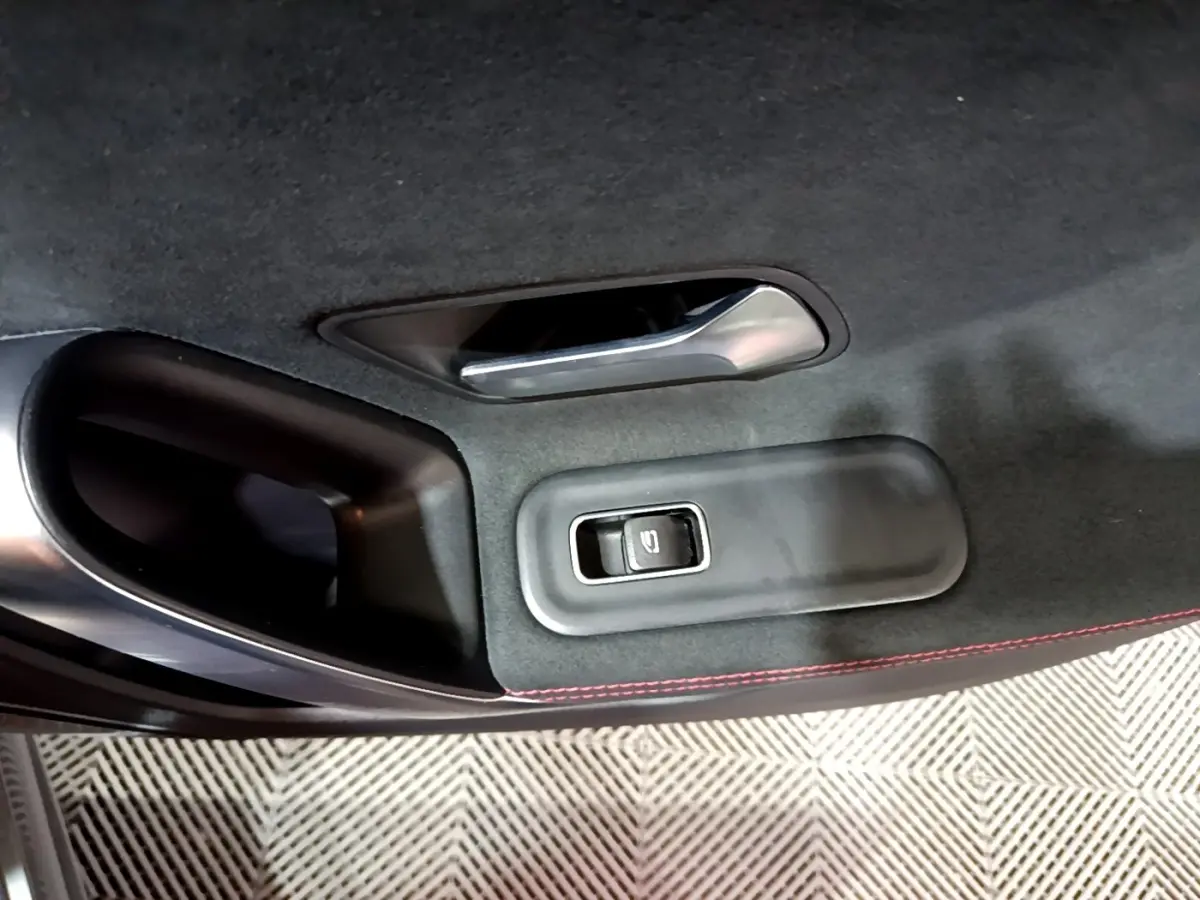 Détail de la porte intérieure côté gauche d’une Mercedes Classe A 250 e AMG Line 2021 gris foncé avec bouton de lève-vitre et surpiqûres rouges.